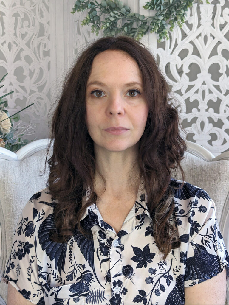 Keen Garrity, sitting in a wing-backed white chair, wearing a bird-print shirt, looking directly at the camera